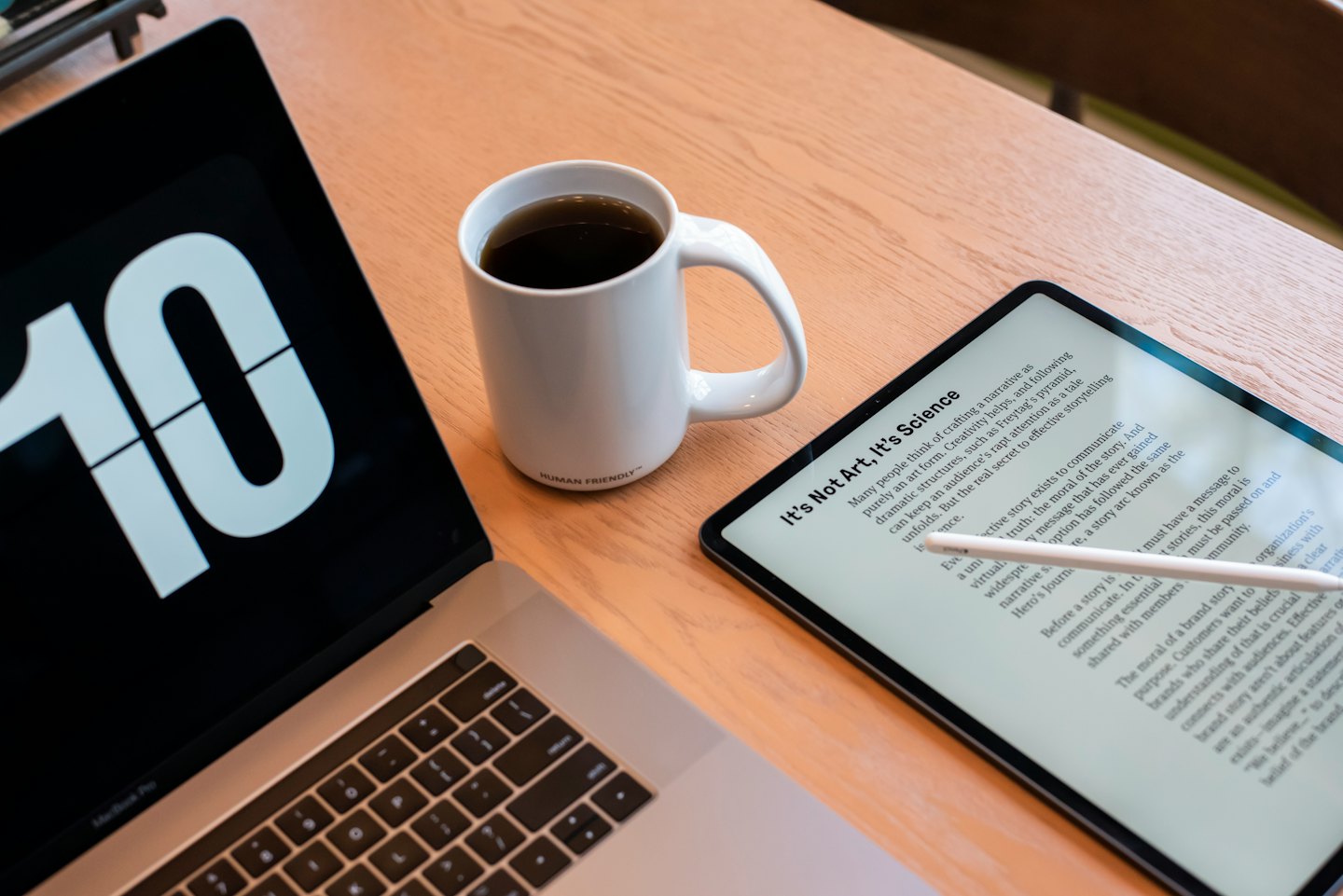 Na ekranie laptopa obok kubka z kawą na biurku widnieje cyfra 10.